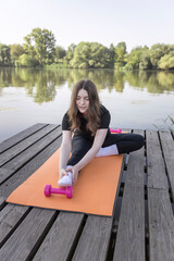 A woman is doing yoga on a mat by a lake