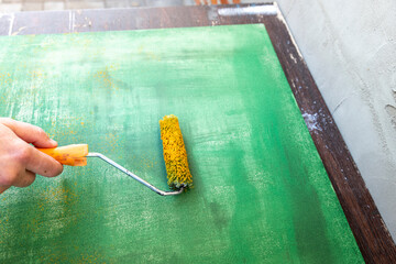 A person is painting a wall with a green color using a roller