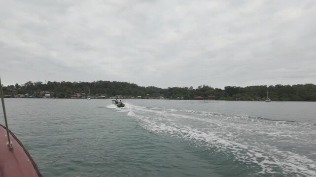 A motorboat cruises on calm waters, leaving a foamy wake under a cloudy sky at Bastimentos Island in Bocas del Toro