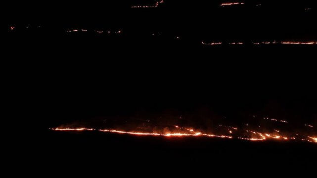 Raging fire at the dry grass meadow. Agricultural field fire burning. Night aerial footage of smoke and flame. Firefighters emergency response. Ecological catastrophe and environmental hazard.