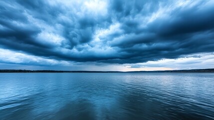 Fototapeta premium Serene lake under dramatic blue clouds, reflecting calm waters and moody skies, perfect for nature and landscape themes.
