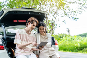 Traveler couple on road trip, man and woman sitting together in car trunk using map in tablet during the trip, Two young boy and girl travel, Two friend traveling on vacation, searching road in map