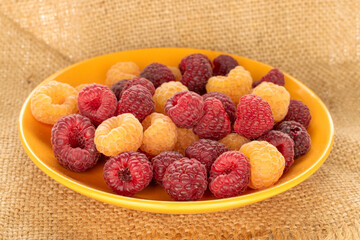 Fresh sweet raspberry with ceramic plate on jute cloth, macro.