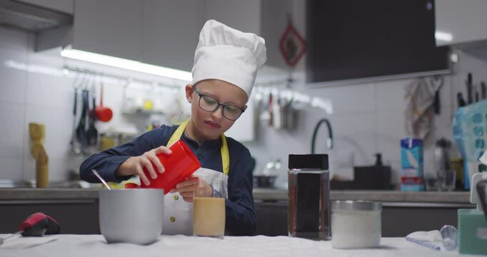 A boy with a chefs hat is making cold instant coffee on a kitchen counter at home.
