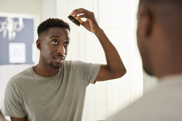 Young African man combing his hair in a bathroom mirror at home