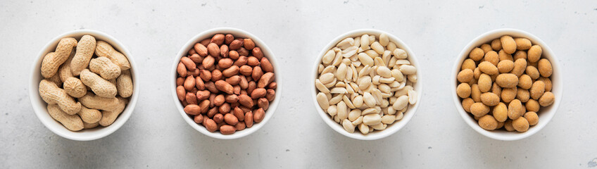 Whole and peeled with blanched and salted peanut nuts in bowls on light background.Top view.