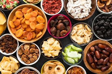 Assorted organic healthy dried sweet berries and fruits snack in various bowl plates on black background.Top view.