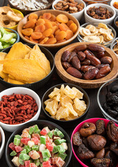 Mix of healthy dried sweet fruits and berries in various bowl plates on black background.Macro.