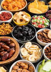 Mix of healthy dried sweet fruits and berries in various bowl plates on black background.Macro.