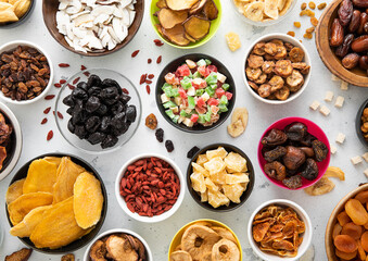 Mix of healthy dried sweet fruits and berries in various bowl plates on light kitchen background.Top view.