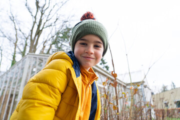 Portrait of a 8 year old Caucasian boy smiling looking at camera on a winter or autumn day wearing a woolen hat and yellow coat