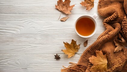 Cozy home desk table with knitted plaid, tea cup, fall leaves on wooden white background. Top view, flat lay, copy space. Autumn composition. Nordic hygge style concept