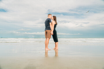 Couple kissing on the beach, holding hands with reflection in wet sand