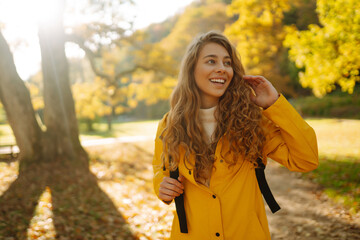 A young woman in a yellow jacket enjoys a sunny autumn day while walking through a park adorned with colorful fall foliage. Relaxation, enjoying, solitude with nature.