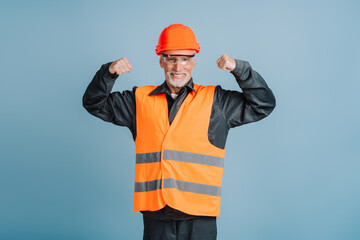 Smiling construction worker wearing hardhat and safety vest flexing muscles