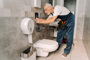 Senior plumber installing toilet cistern water supply system