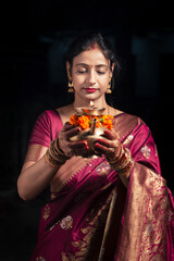 A traditional Indian woman holds a decorated brass Karwa with closed eyes for Karwa Chauth, an Indian tradition.