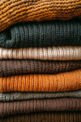 stack of knitted sweaters in various shades, arranged neatly and stacked on top of each other. The colors include warm browns, soft oranges, deep greens, and light blues, creating an inviting texture 