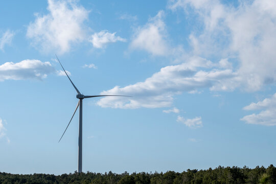 A single wind turbine stands tall under a blue sky with scattered clouds, showcasing renewable energy in harmony with the natural landscape in Tarragona Spain