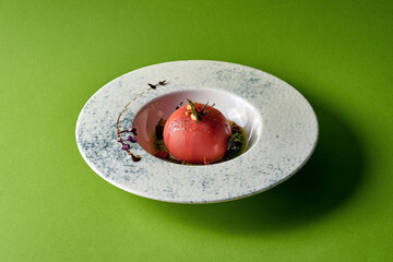 tomato, garnished with pine nuts and herbs, served on a white plate against a green background.