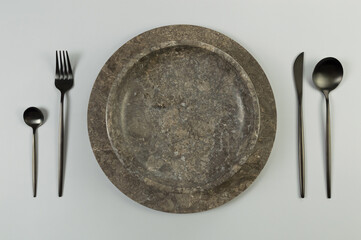 Top view of brown marble tray and plate, black cutlery on grey background. Food presentation, stone...