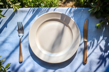 The image presents a table setting with a white plate, a fork, a knife, and a napkin, all arranged on a blue tablecloth