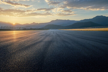 Fototapeta premium Empty straight racetrack at sunrise with mountain range in the background. High quality photo