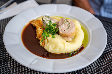  Chicken roulade on mashed potato and sauce, sprouted pea shoot on white plate.