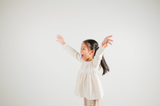 A jubilant kid girl raises her fists in celebration of her success, saying yes with excitement. Asian portrait of a happy young kindergarten child in a studio shot on a white background, winning