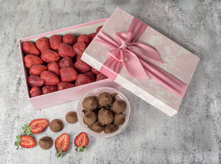 A pink gift box with red, natural strawberries and chocolates nearby, for congratulations, a postcard, for a holiday.