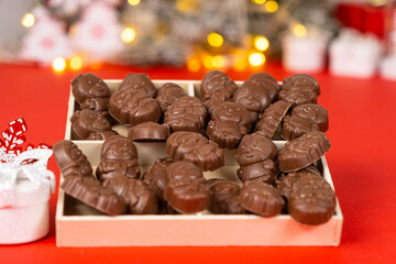 Chocolates in the shape of Christmas figures in the wooden box on the red background