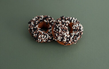 two donuts with sprinkles of white, milk and dark chocolate balls on a light background, cover, dessert decoration, chocolate balls, sweet pastries, donut day, Fat Thursday
