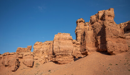 the grandeur of towering red sandstone cliffs against a clear azure sky, a serene, untouched wilderness in late summer or early fall due to the warm lighting.