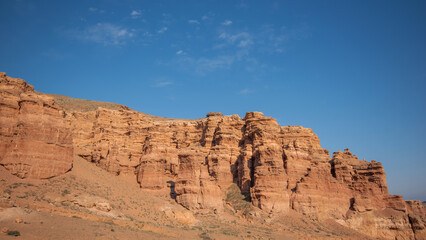Fototapeta premium a striking range of massive red sandstone formations under a vast blue sky, hinting at a tranquil desert setting in the warm, gentle light of a late summer afternoon