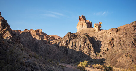 a striking desert scene with rugged mountains and a distinctive rock formation that resembles a castle, set against a clear sky and dotted with green desert shrubs