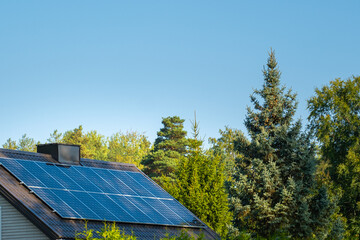 solar panels on home roof against blue sky and trees. green energy concept.