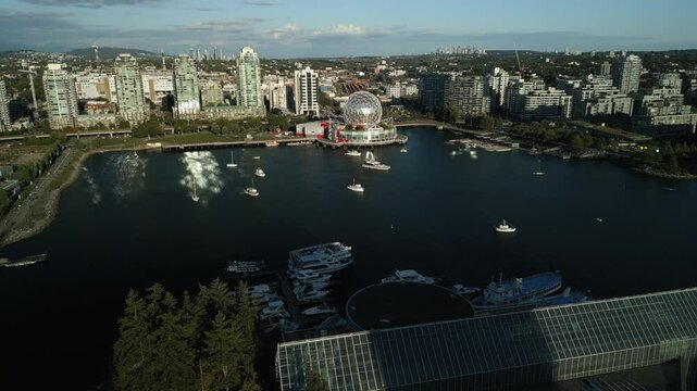 wide drone orbit around iconic Scienceworld building on the edge of False Creek harbour in downtown Vancouver, Canada during a bright sunset in summer with boats sat on the water