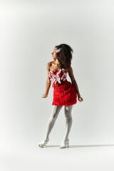 A young woman with curly hair exudes confidence, showcasing her stylish red ensemble on a minimalist background.