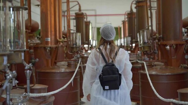 A female tourist wearing disposable gown and cap touring Ouzo distillation area with copper alembics that traditionally produce Ouzo of Plomari at The World of Ouzo museum