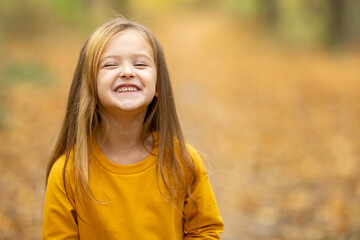 Smiling little girl in yellow dress has fun while walking in the autumn park in nature. Child spend time in the forest in fall.