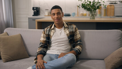 Obraz premium Portrait at home relaxing ethnic man smiling indoors looking at camera at comfortable couch at own estate new rent house healthy African American biracial guy male smile toothy dental at sofa headshot