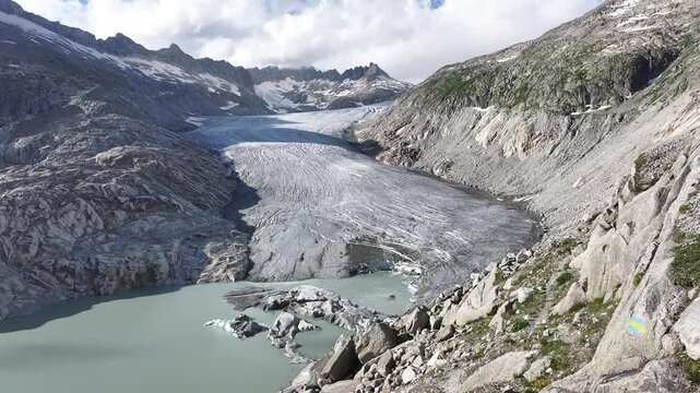 Drone pulls back from crystal clear lake surrounded by white rocky mountains at Rhonegletscher, Furkapass, Switzerland.