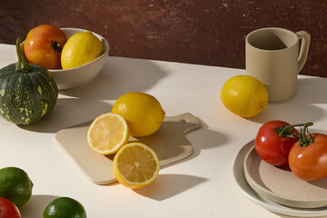 Fresh fruits typical of autumn decorated with ceramic utensils on a brown background. Green pumpkin, lemons and lime, fresh ripe tomatoes. Autumn concept