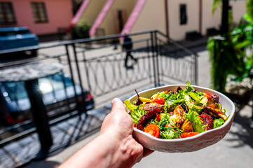 hand holding a bowl of fresh salad with mixed greens, cherry tomatoes, and grilled chicken, set...