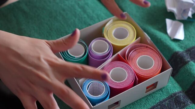 A box of colorful bandages is opened and displayed on a green cloth. The box contains a variety of bandages in different colors, including blue, green, yellow, and red