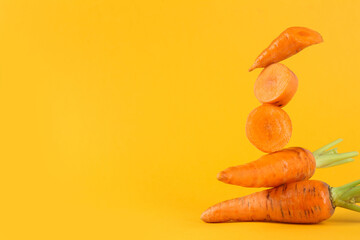 Whole and cut fresh carrots on orange background, space for text