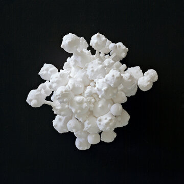 a ball and stick model of one zwitterionic form of creatine, made of white clay. Floating against a completely black background.
