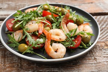 Delicious shrimp salad with tomato and olives on wooden table, closeup