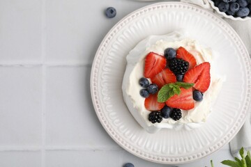 Pavlova cake (meringue dessert) with whipped cream, fresh berries and mint on white tiled table, top view. Space for text