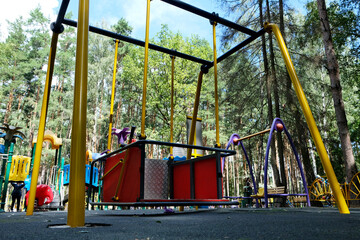 Swings for disabled children in wheelchairs in a city park among trees